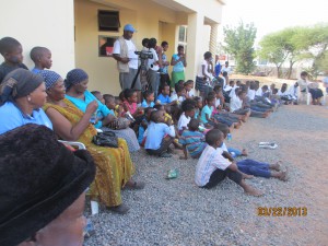 The community is watching the skit and listening to the speakers